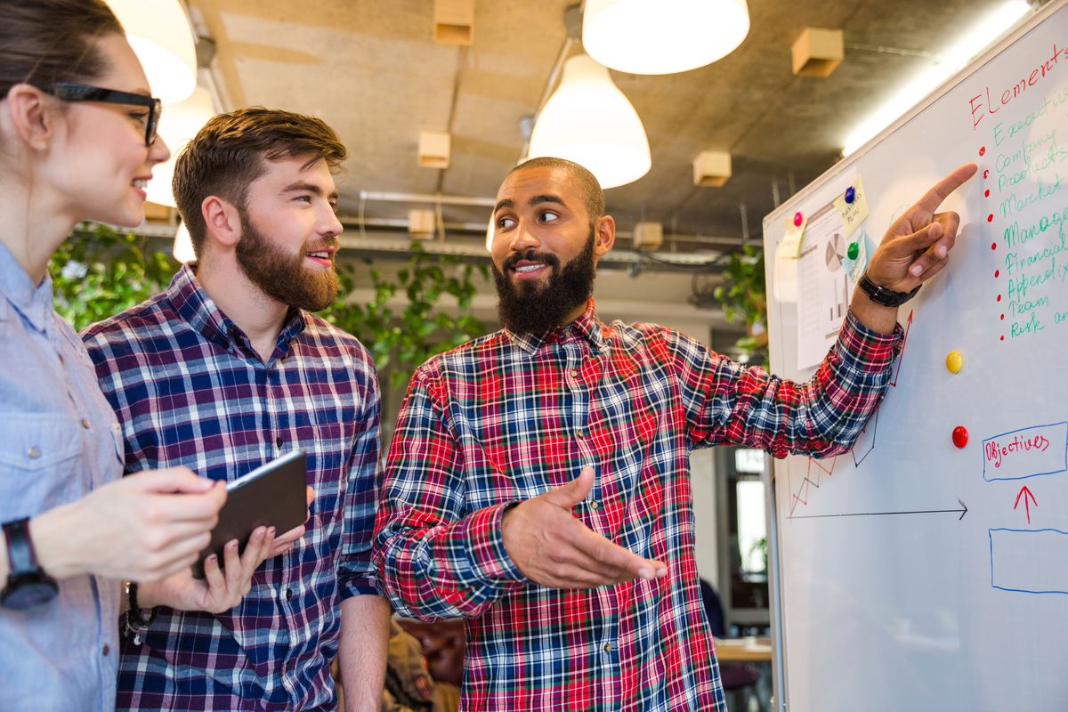 zur Vergrößerungsansicht des Bildes: Mitarbeitende vor Whiteboard