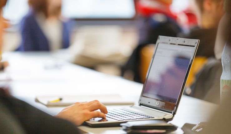 A laptop is in focus with the seminar participants blurred in the background.