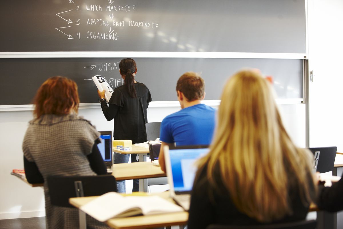 enlarge the image: Lehrerin schreibt etwas an die Tafel, während Schüler und Schülerinnen aufmerksam schauen. Foto: Colourbox