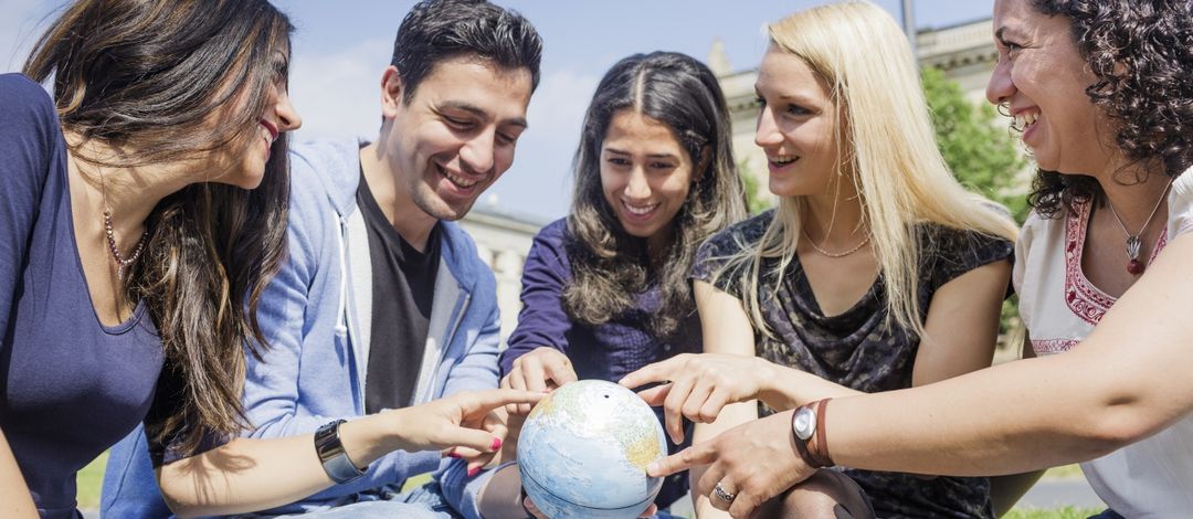 Foto: Eine Gruppe internationaler Studierender betrachtet eine Weltkugel und zeigen sich gegenseitig ihre Heimatländer