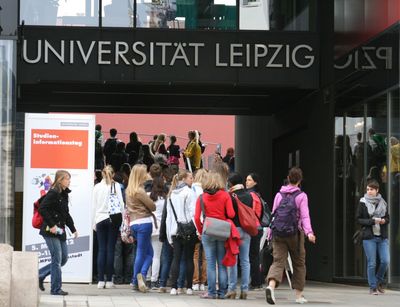 Foto: Junge Menschen stehen in einer Schlange vor dem Eingang zum Universitätsgelände. Am Eingang steht ein Poster zum Studieninformationstag.