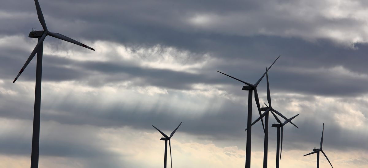 Photo of 6 wind turbines against a cloudy sky. 