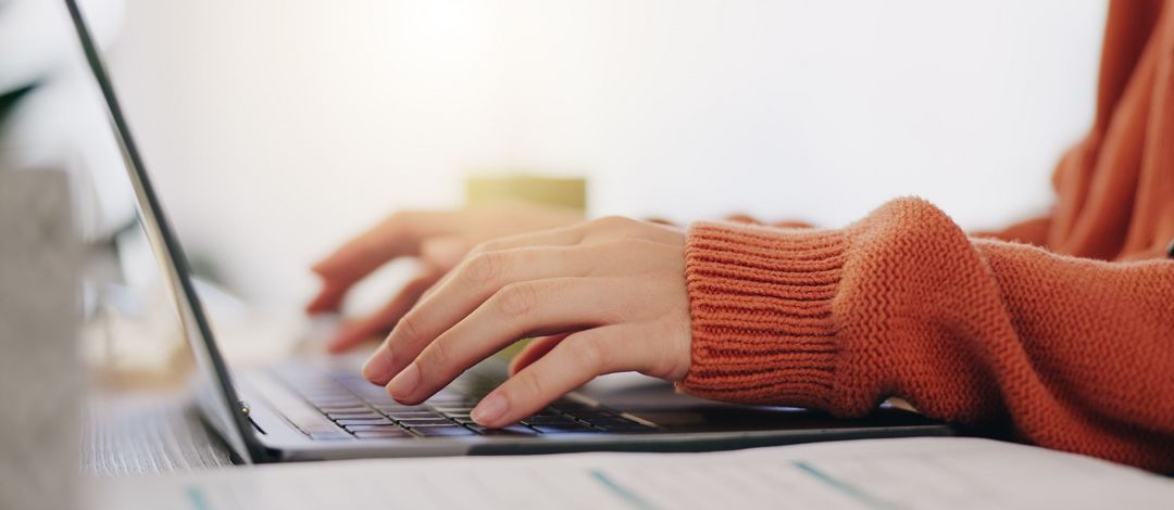 Person schreibt auf Tastatur vom Laptop, nur die Arme und Hände sind sichtbar