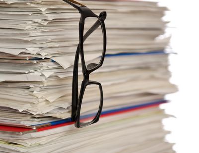 A stack of papers, with reading glasses hanging down.