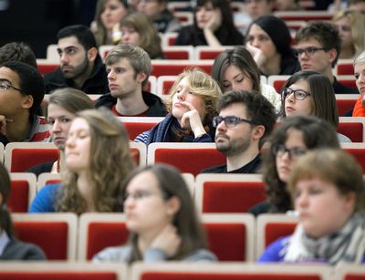 A group of students sit in a lecture hall and listen attentively to a lecture.