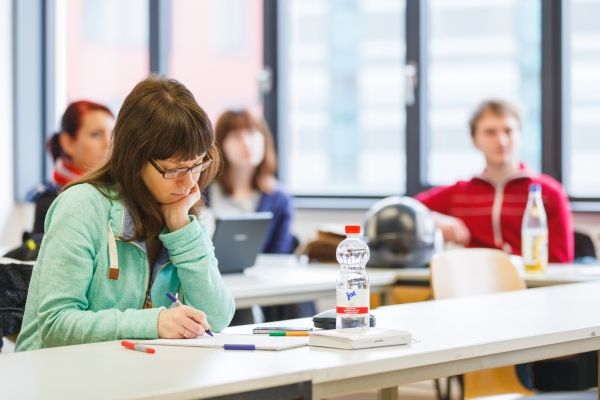 Man sieht eine Gruppe von vier Studenten im Seminar. Eine Studentin mit grünem Pullover sitzt im Vordergrund und betrachtet ihre Notizen.
